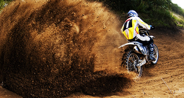 A motocross biker trowing up a large trail of dirt from his rear wheel