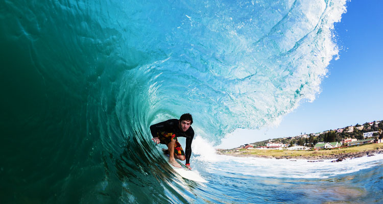 A surfer in the middle of the barrel of a wave off of a sandy beach with cottages
