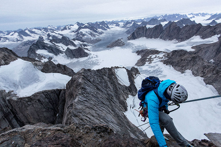 A climber in a blue Arc'teryx brand jacket in front of an amazing mountain range vista