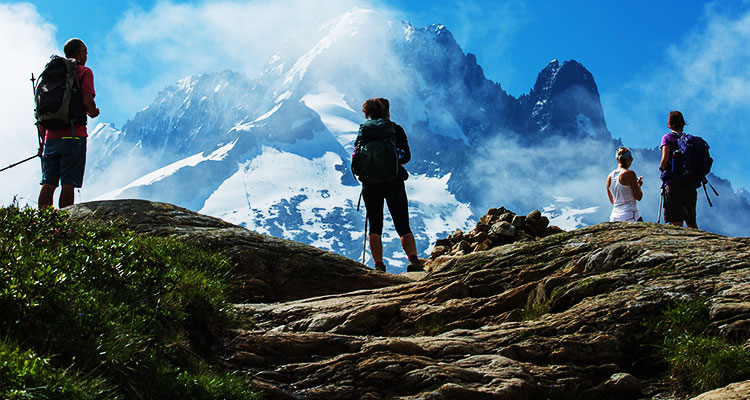 Four hikers on a mountain looking at the peak of a snow capped mountain