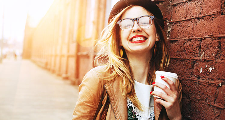 A trendspotting woman with a beret, hipster glasses, a camel leather jacket and a artisan coffee in hand