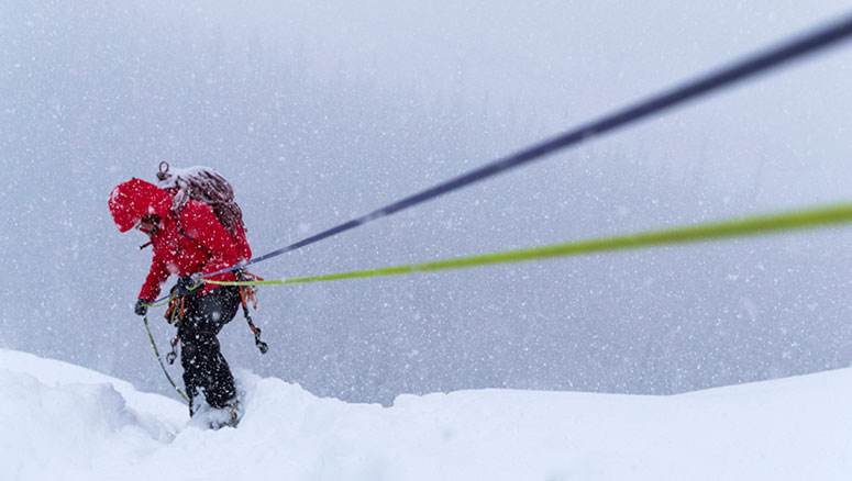 A rock climber wearing an Arc'terx brand jacket climbing up a rope in a snow storm