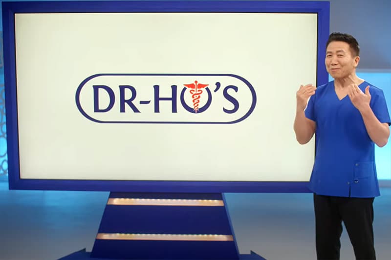 Dr Ho, a doctor in blue scrubs, standing in front of a monitor displaying his logo.