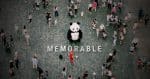 Person in a panda suite standing in front of the word "memorable" in a crowd.