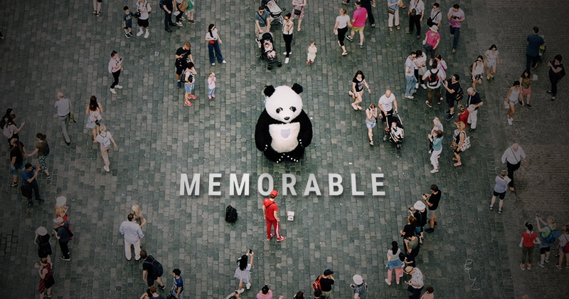 Person in a panda suite standing in front of the word "memorable" in a crowd.